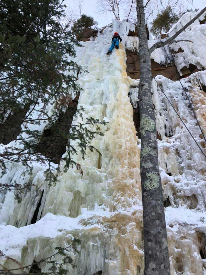 Wide angle shot of a Girl Scout climbing a frozen waterfall.