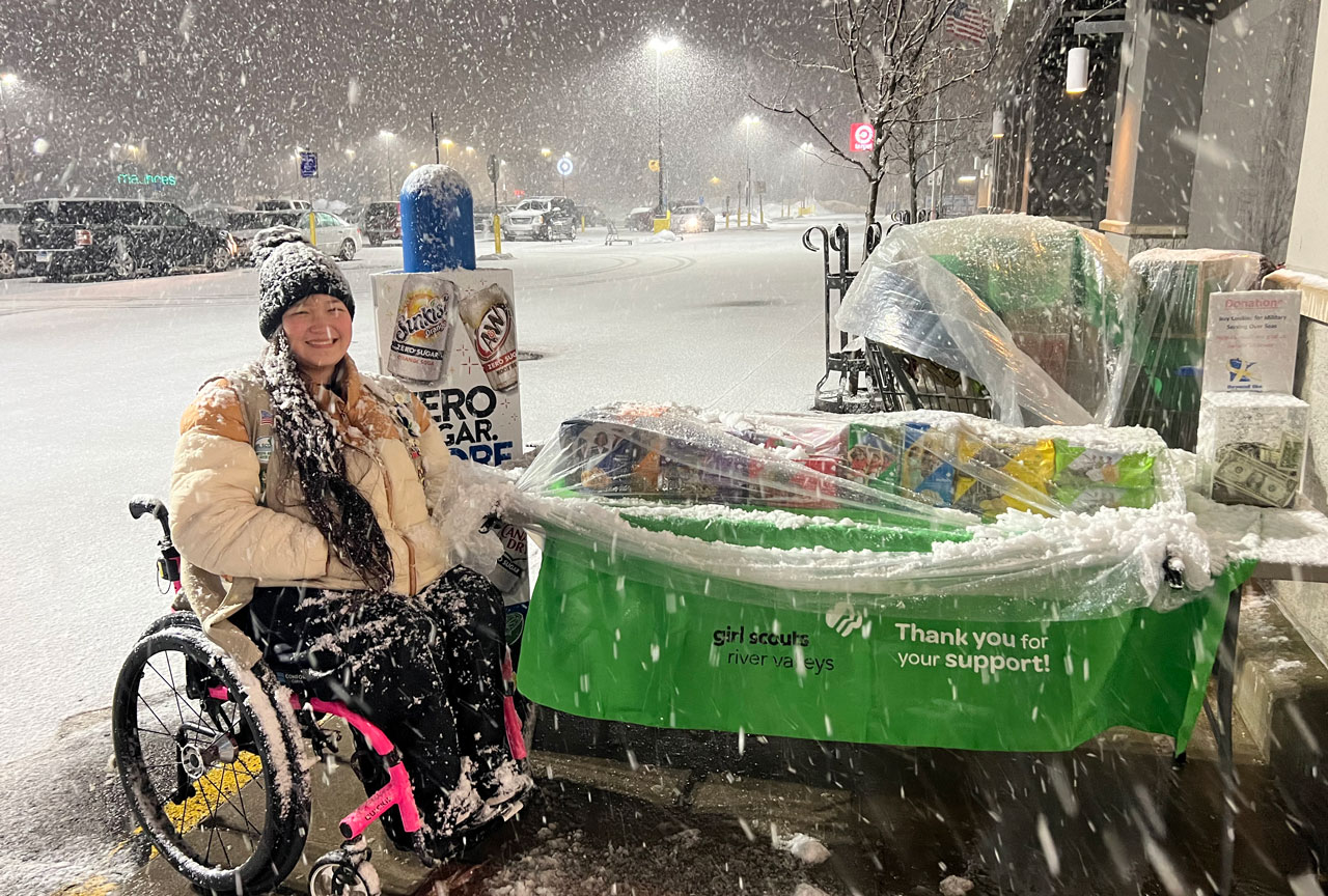 Girl Scout managing her cookie booth with snow falling